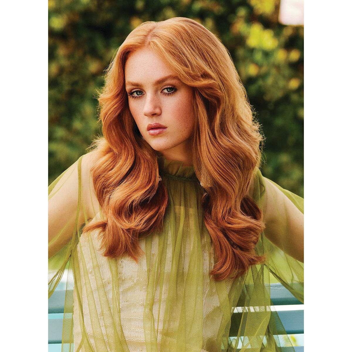 Red-haired woman with soft, flowing curls draped over a sheer lime green top, showcasing a simple yet elegant hairdo.